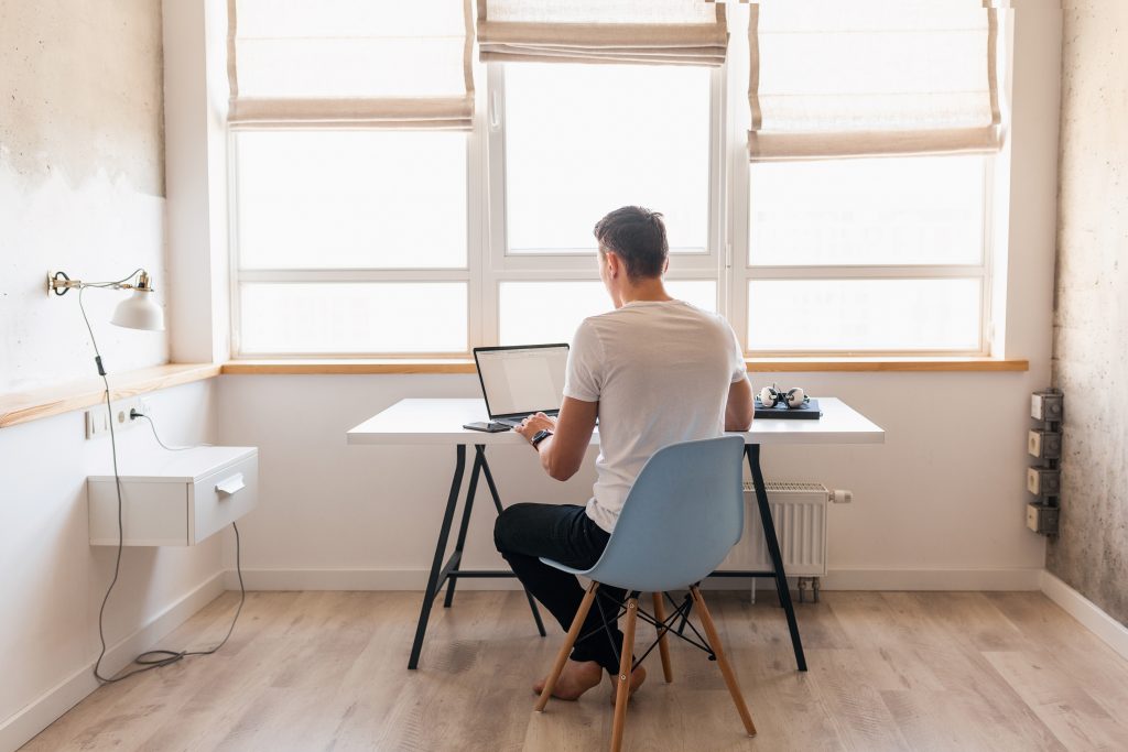 modern young handsome man in a casual outfit sitting at table working on laptop, freelancer at home, view from back